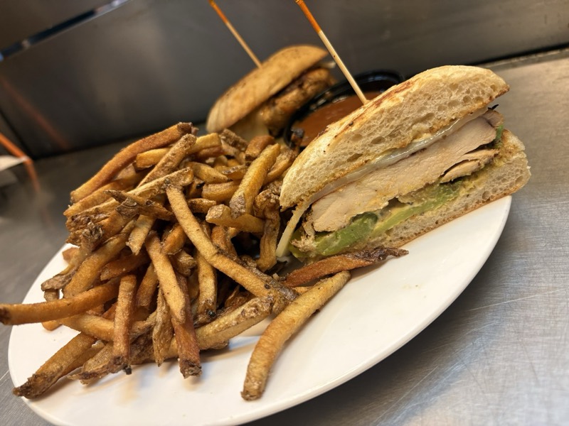 Grilled chicken sandwich with avocado and melted cheese, served with hand-cut fries