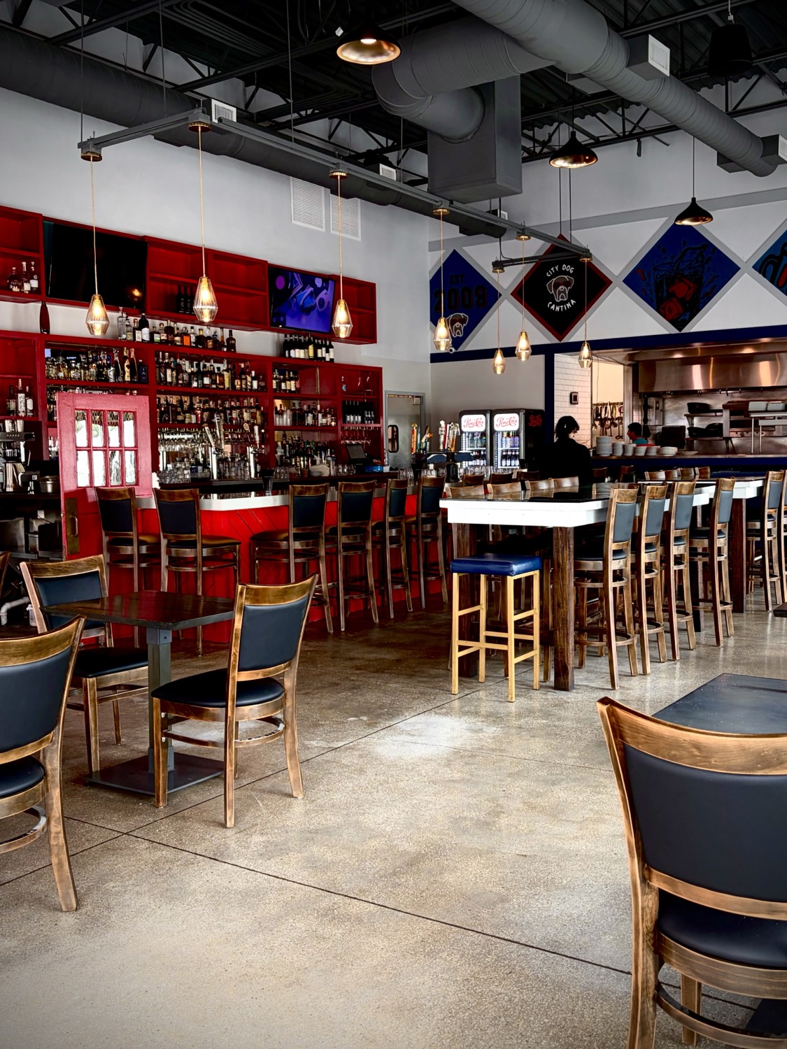 Inside City Dog Cantina: the red back bar, high-top seating, and the open kitchen